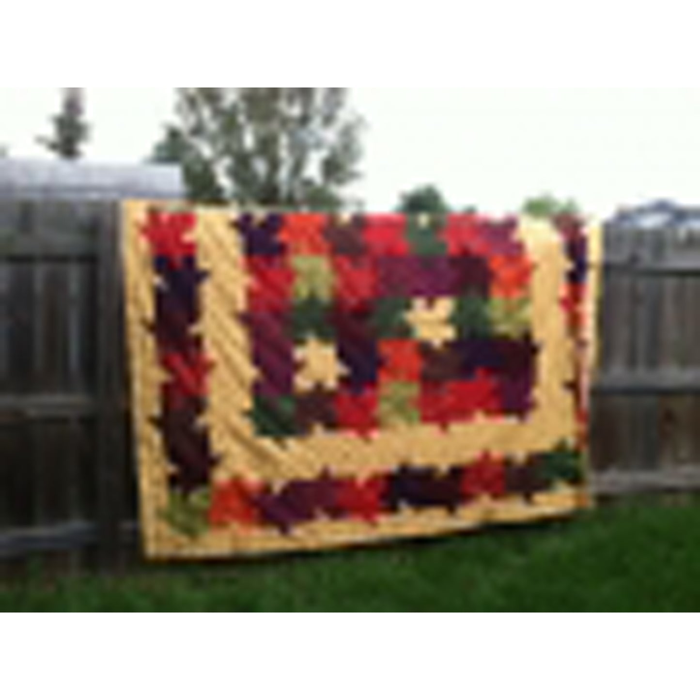 Quilt hanging over a fence. Beautiful quilt of colorful leaves on a tan background.