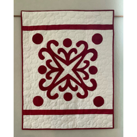 Red and white quilt hanging on wall with intricate snowflake design in red with cirlces around the edges on white background.