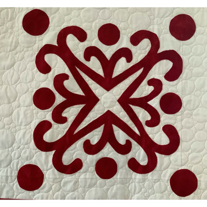 Red and white quilt with intricate snowflake design in red with cirlces around the edges on white background.