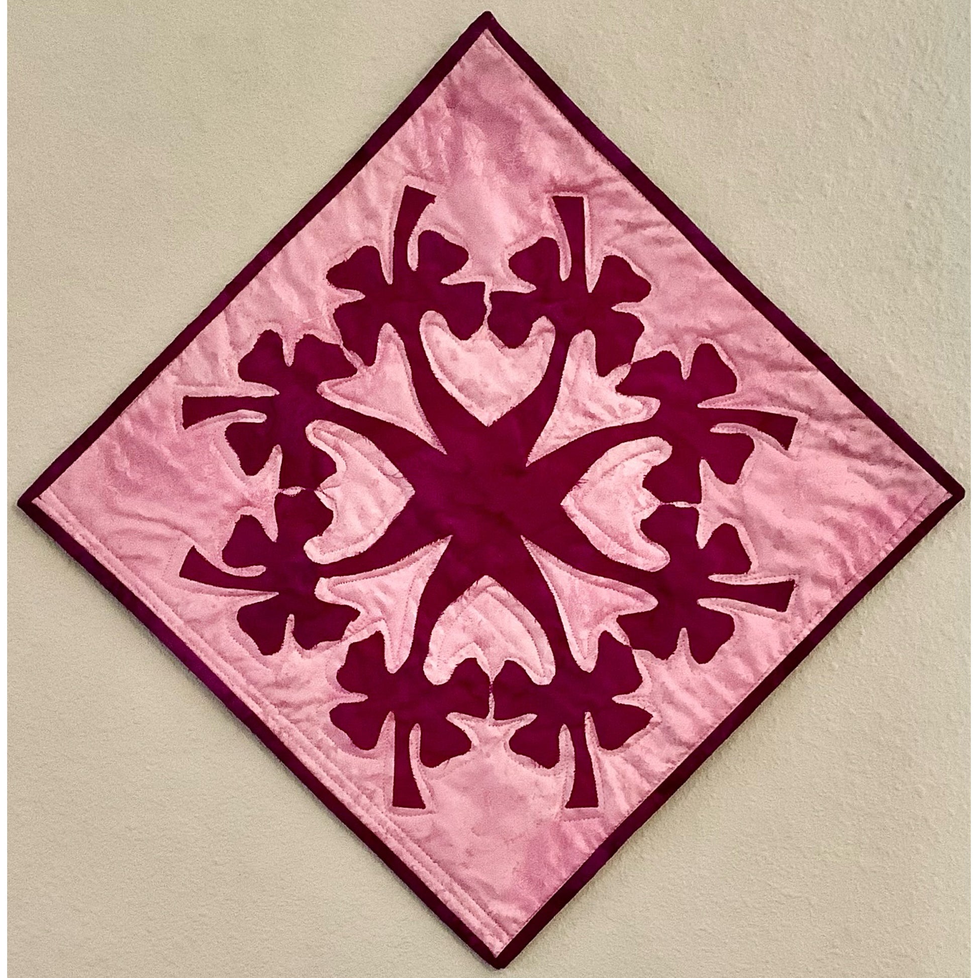 Pink quilt block with floral pattern applique design in red in the middle in a circle with flowers coming out of a main center.