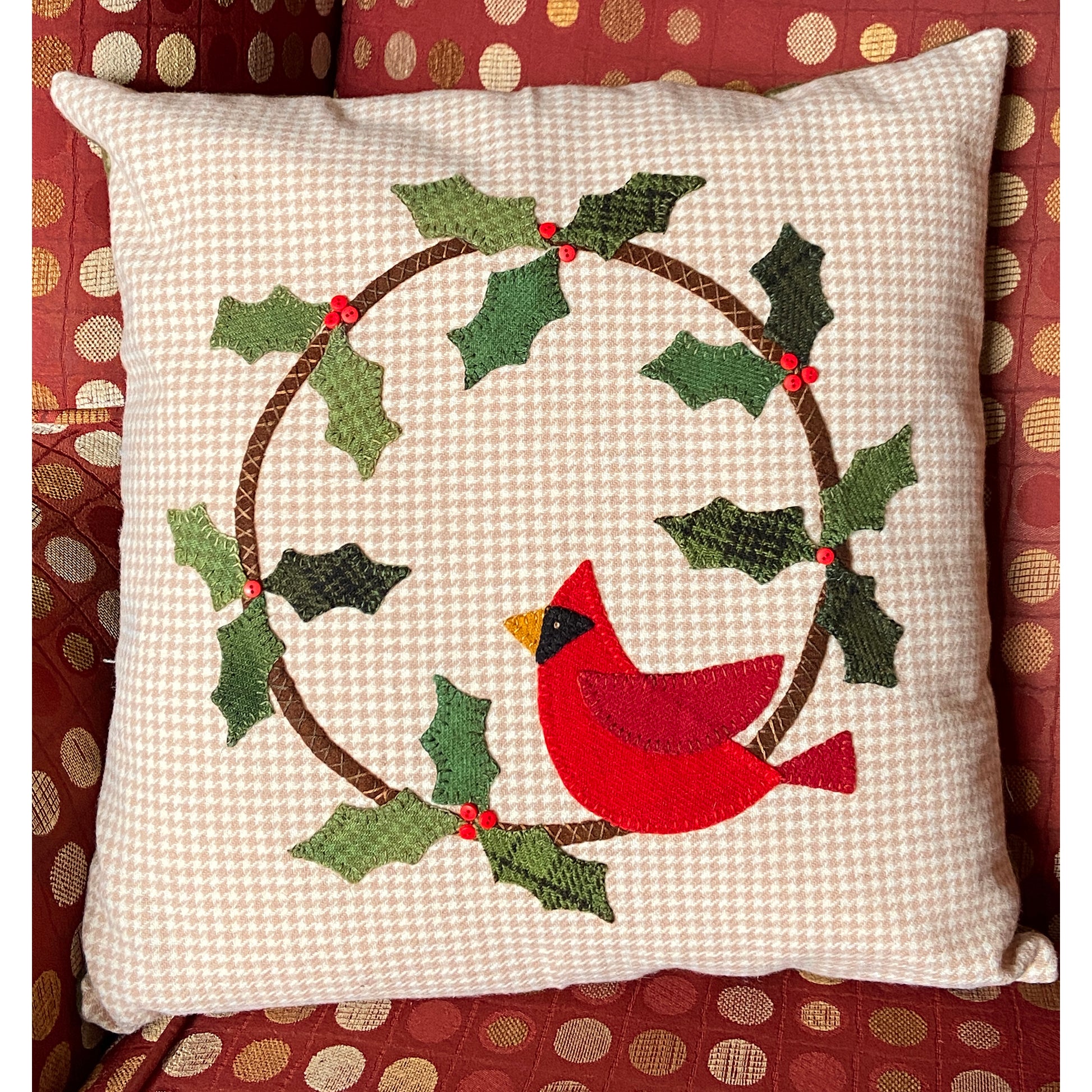 A festive red cardinal pillow adorned with holly leaves, perfect for adding holiday cheer to any space.
